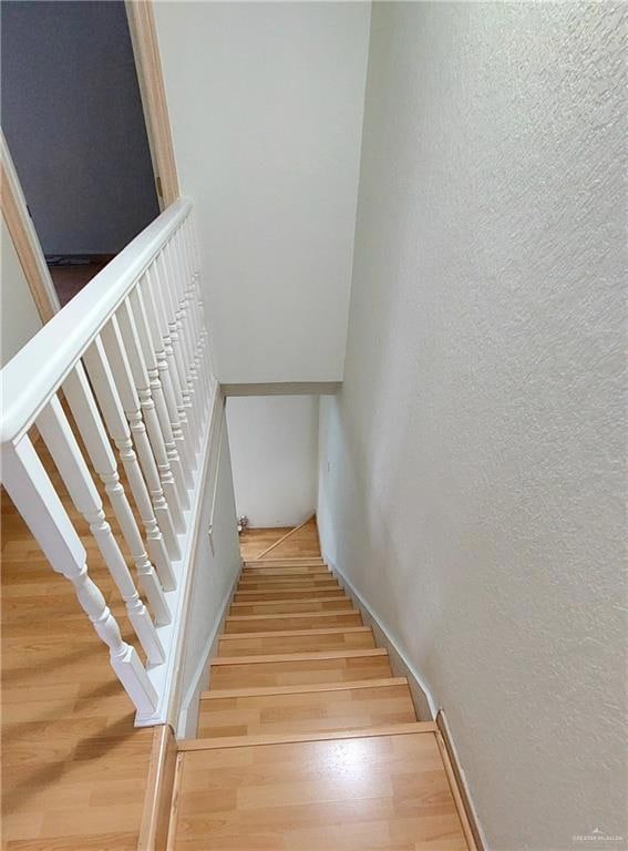 Stairs with wood finished floors and a textured wall