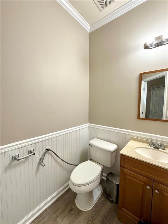 Half bath featuring wood finished floors, a wainscoted wall, vanity, and crown molding