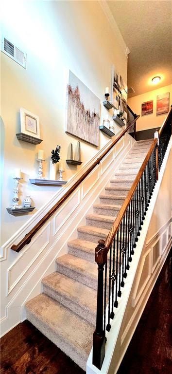 Stairway featuring wood finished floors, ornamental molding, and a textured ceiling