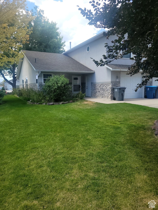 Ranch-style home with concrete driveway, stone siding, a front lawn with mature trees.