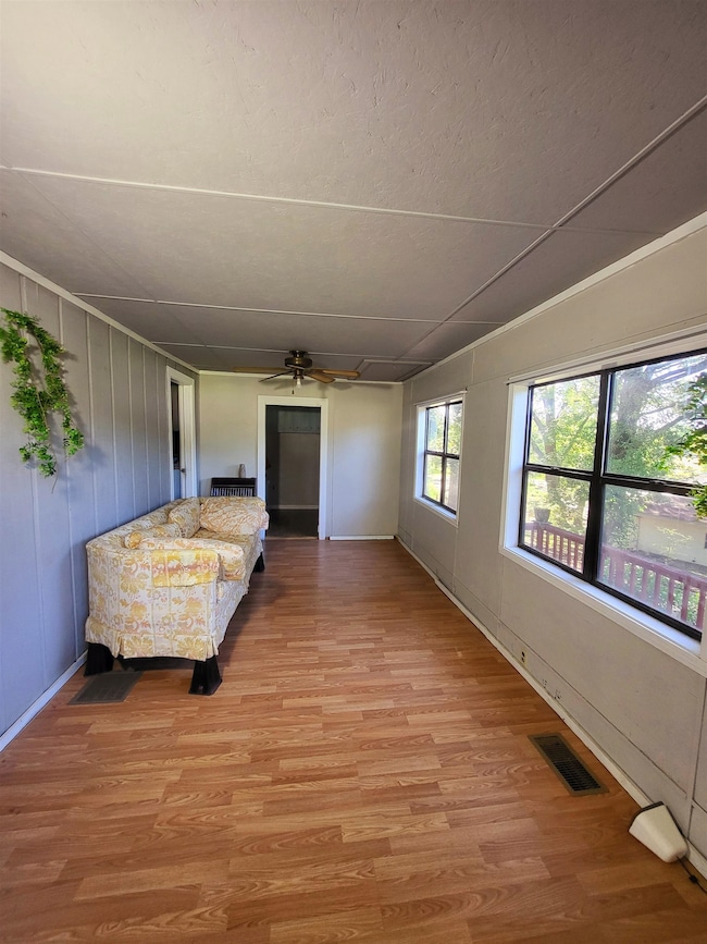 Living room with light wood-style floors, a ceiling fan, and baseboards
