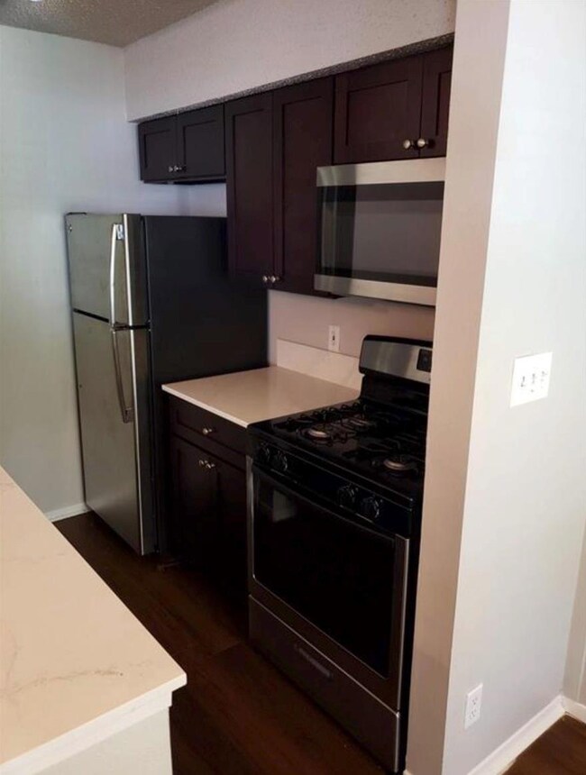 Kitchen with gas stove, stainless steel microwave, dark wood-type flooring, light countertops, and a textured ceiling