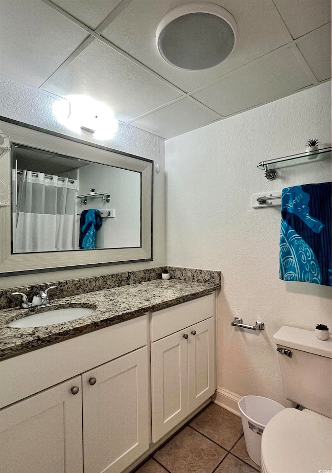 Full bathroom with curtained shower, vanity, dark tile patterned floors, and a textured wall