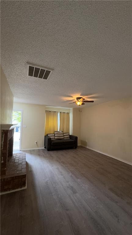 Unfurnished living room featuring dark wood-type flooring, a fireplace, a textured ceiling, and ceiling fan
