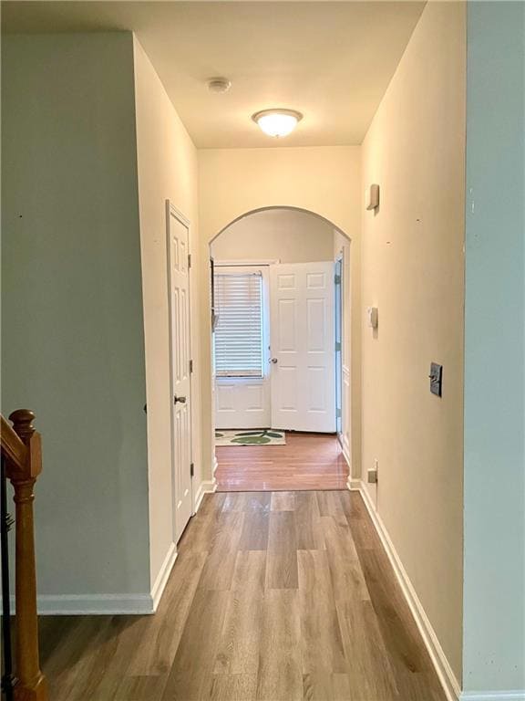 Corridor featuring wood finished floors, arched walkways, and baseboards