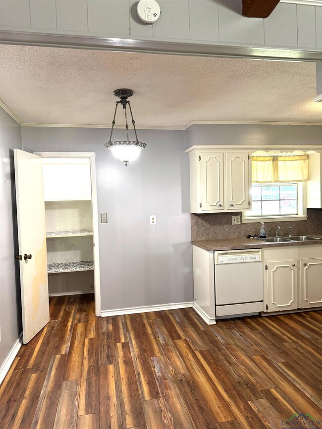 Kitchen featuring dishwasher, ornamental molding, a textured ceiling, dark countertops, and white cabinetry