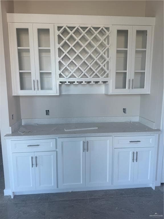 Bar area featuring white cabinets, glass insert cabinets, and light stone countertops