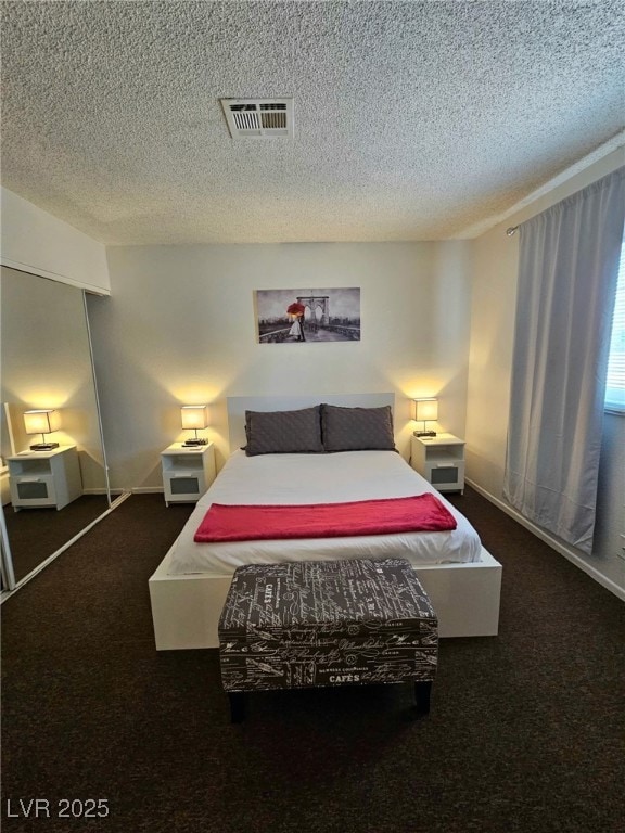 Bedroom with dark carpet, a textured ceiling, and a closet