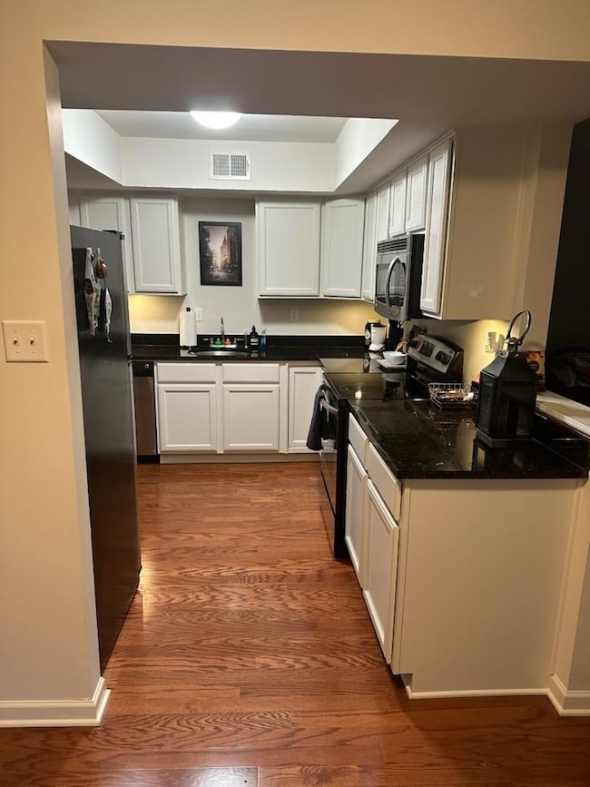 Kitchen featuring stainless steel appliances, dark wood-style floors, dark countertops, and white cabinets
