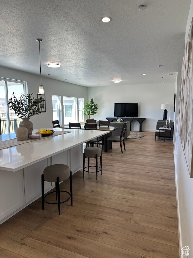 Kitchen featuring a textured ceiling, light wood finished floors, plenty of natural light, decorative light fixtures, and a breakfast bar area
