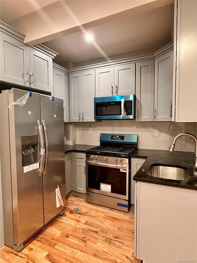 Kitchen with stainless steel appliances, dark stone counters, and light wood-style floors