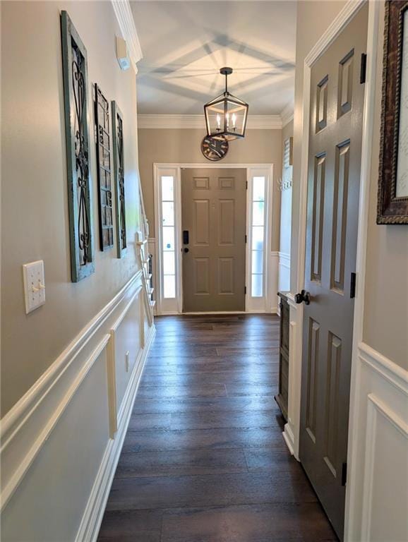Entryway featuring crown molding, a decorative wall, a chandelier, dark wood-type flooring, and a wainscoted wall