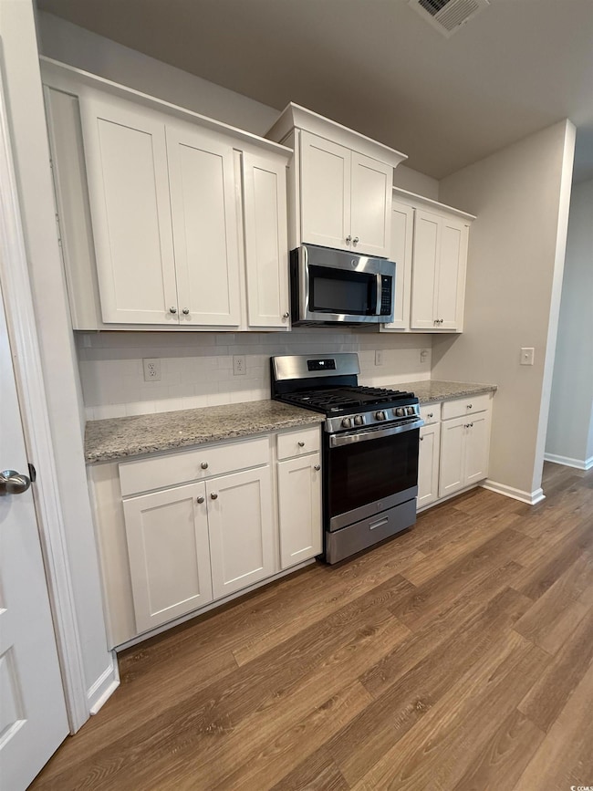 Kitchen with stainless steel appliances, white cabinetry, dark wood-style flooring, and light stone countertops