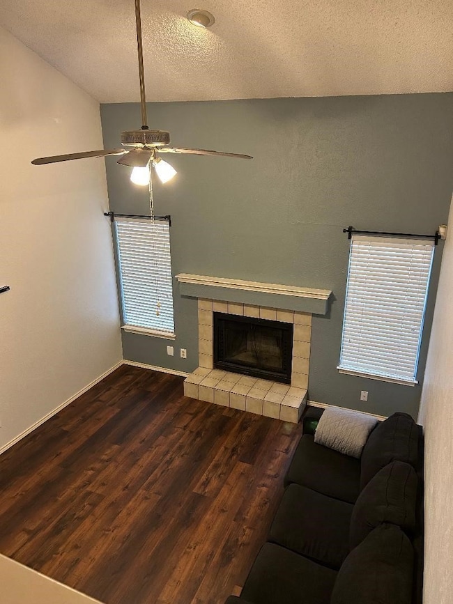 Living area featuring a textured ceiling, a tiled fireplace, wood finished floors, a ceiling fan, and vaulted ceiling