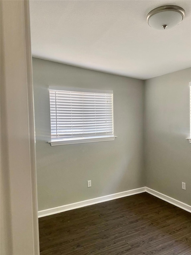 Unfurnished room with baseboards and dark wood-style floors
