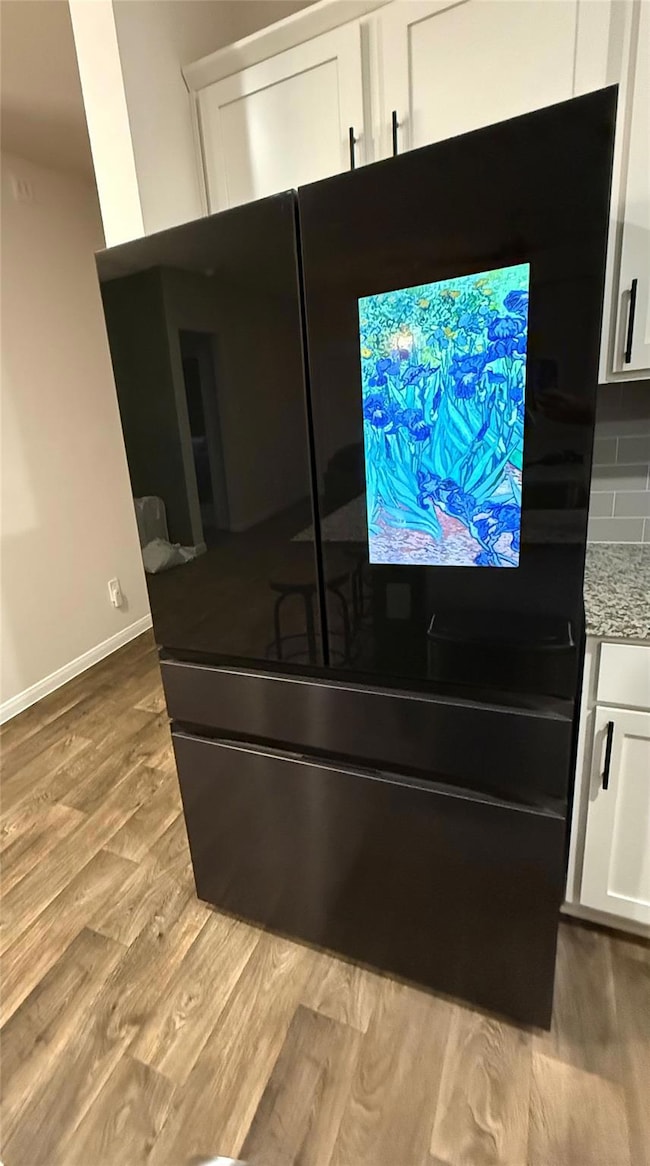 Kitchen view of freestanding refrigerator, white cabinetry, light stone countertops, and light wood-style flooring