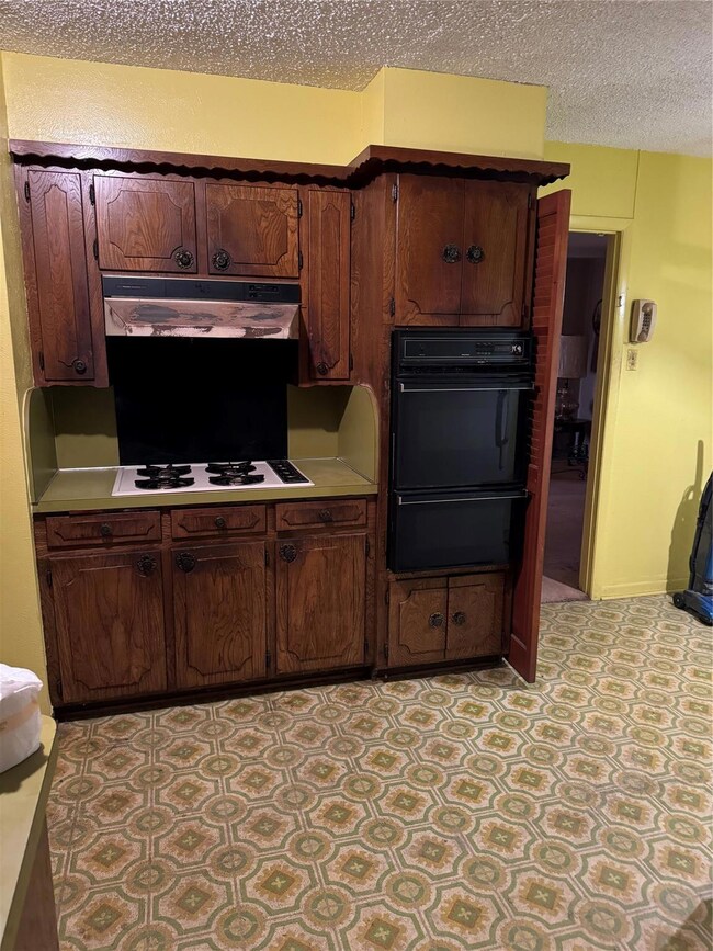 Kitchen with a textured ceiling, cooktop, dark bro