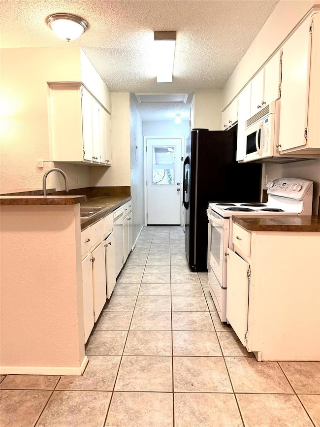 Kitchen with white appliances, a textured ceiling, dark countertops, light tile patterned floors, and white cabinetry