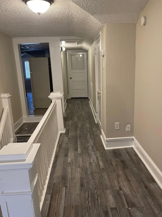 Hall featuring a textured ceiling, dark wood-style