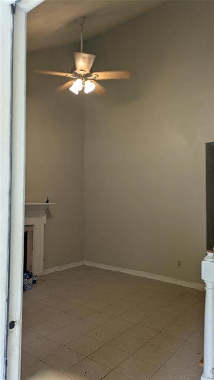 Empty room featuring vaulted ceiling, ceiling fan, and light tile patterned floors