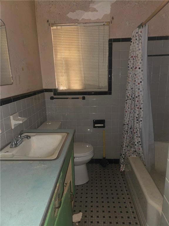 Full bathroom with vanity, shower / bath combo, tile walls, and wainscoting