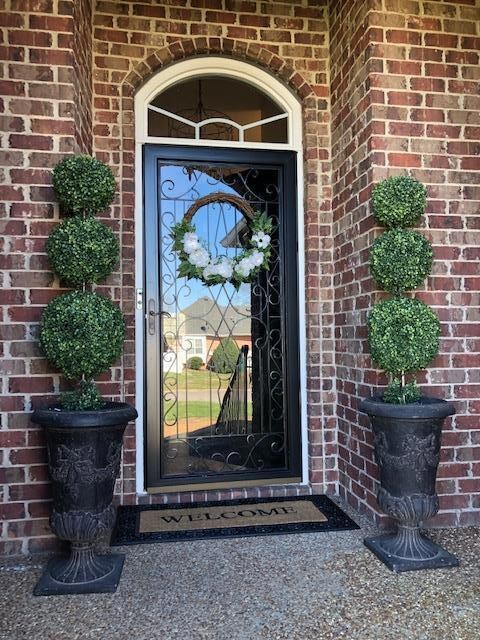 Guests are Greeted with this Elegant Custom Iron Storm Door with Arched Window! The Covered Porch has Two Insets for Benches or Decorative Plants!