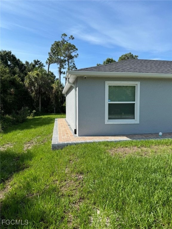 View of side of property with stucco siding, a yard, and a patio area