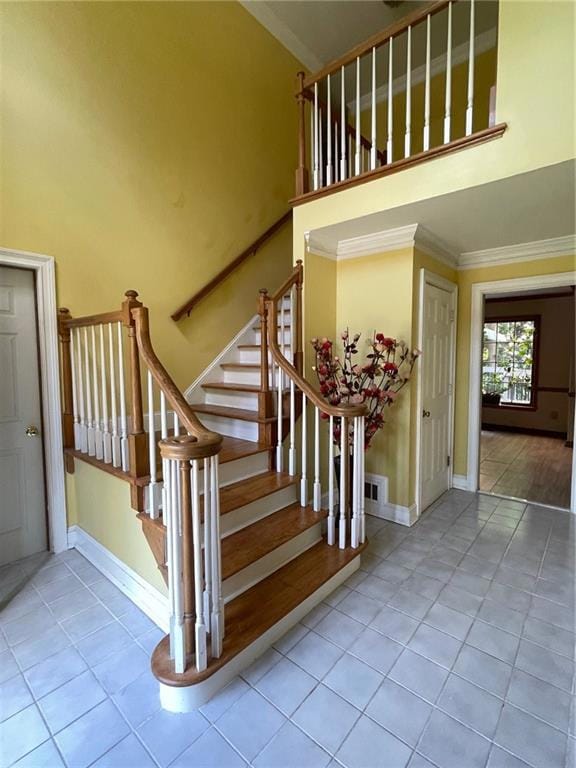 Stairway featuring a high ceiling, tile patterned flooring, crown molding, and baseboards