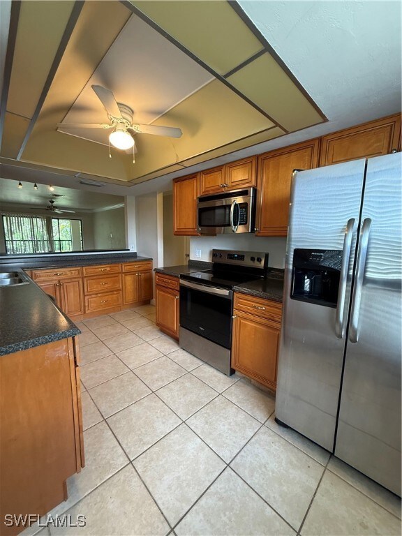 Kitchen featuring refrigerator, electric range, light tile patterned flooring, a ceiling fan, and brown cabinets