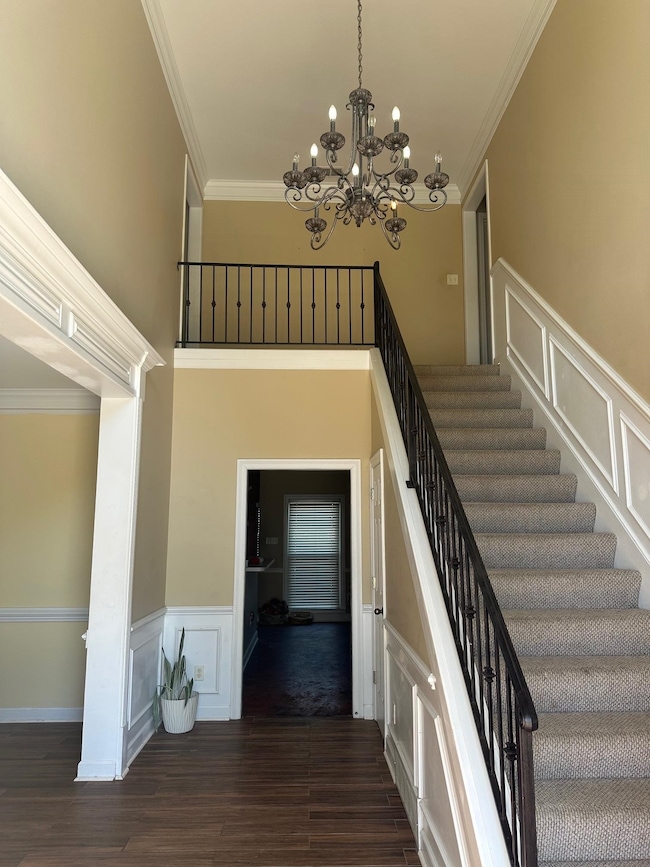 Stairway with a decorative wall, wainscoting, crown molding, wood finished floors, and a chandelier