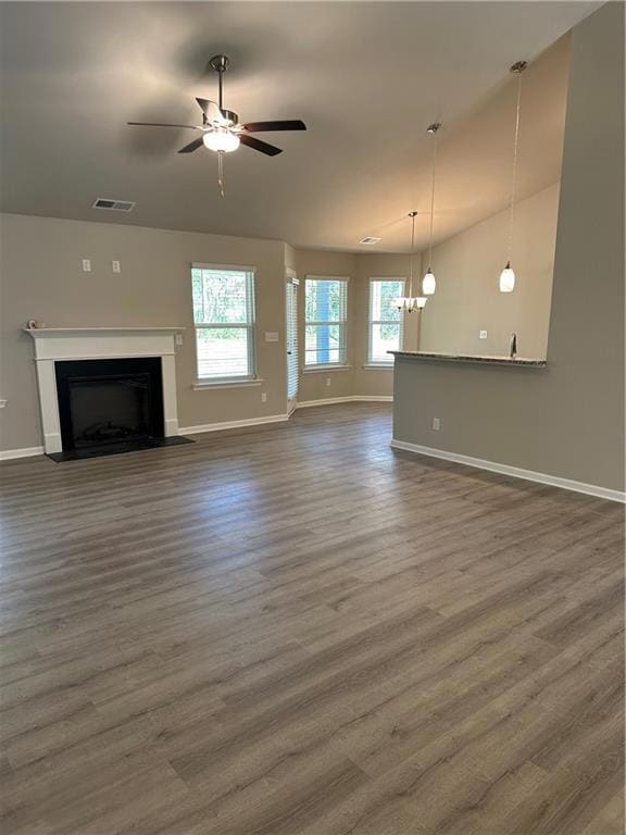 Unfurnished living room featuring vaulted ceiling, dark wood-style floors, a fireplace, a ceiling fan, and a chandelier