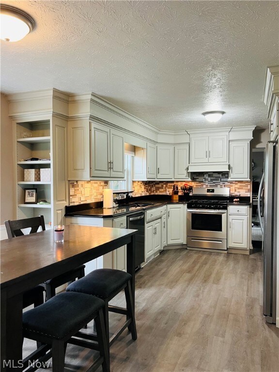 Kitchen with custom exhaust hood, stainless steel appliances, light hardwood / wood-style flooring, a textured ceiling, and backsplash