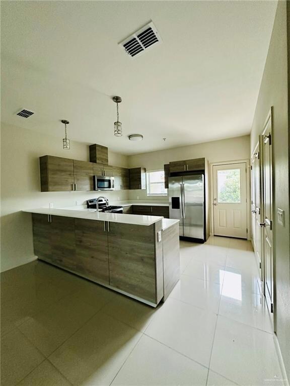 Kitchen featuring light tile patterned floors, a peninsula, stainless steel appliances, modern cabinets, and decorative light fixtures