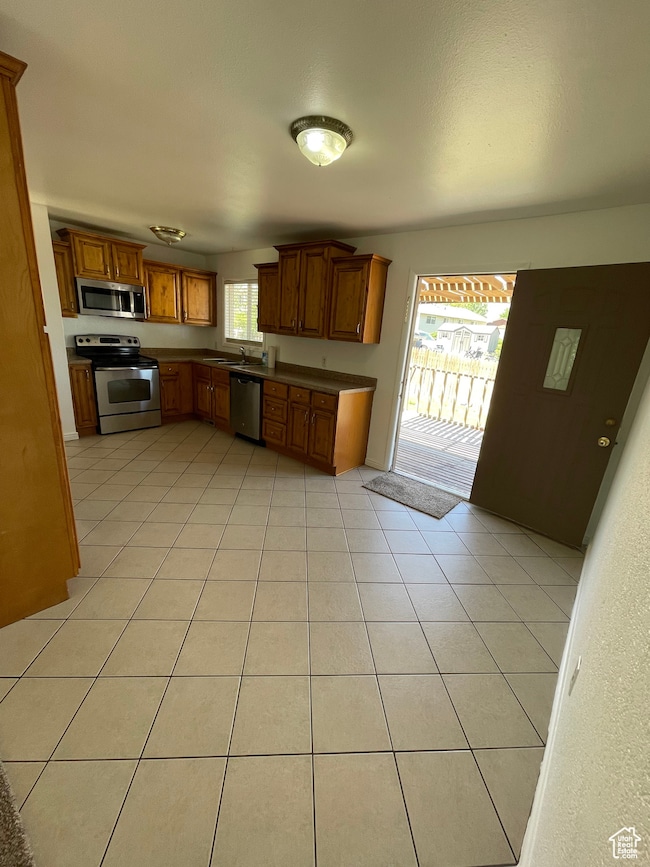 Kitchen featuring stainless steel appliances, dark countertops, light tile patterned flooring, and brown cabinets