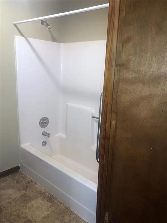 Full bath with shower / washtub combination and dark stone finish flooring