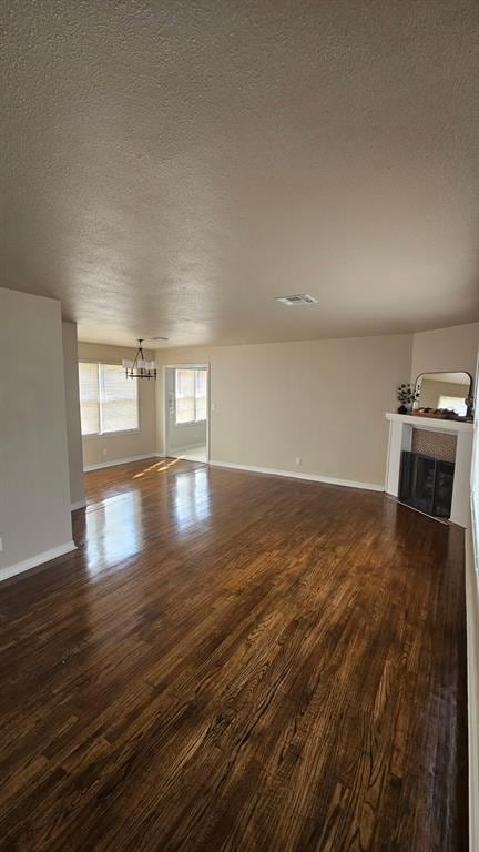 Unfurnished living room featuring a textured ceiling, a chandelier, dark wood-style floors, and a fireplace