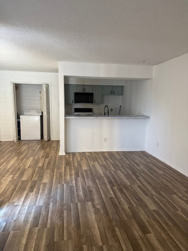Unfurnished living room featuring washer / clothes dryer, dark wood finished floors, and a textured ceiling