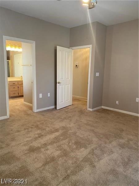 Unfurnished bedroom with baseboards, ensuite bathroom, and light colored carpet