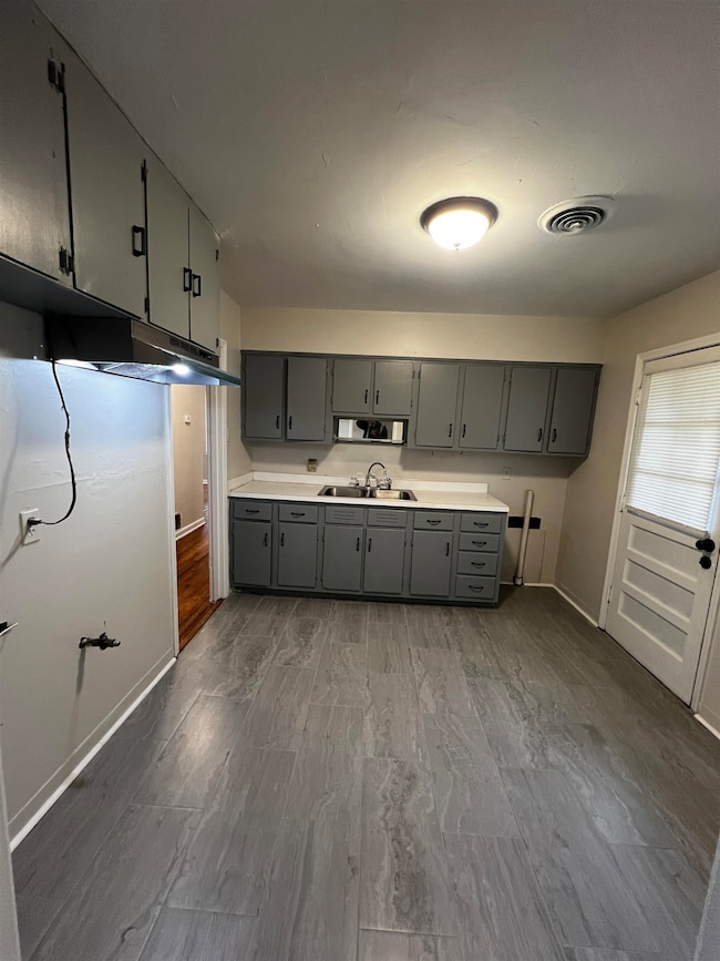 Kitchen featuring gray cabinetry, a sink, baseboar