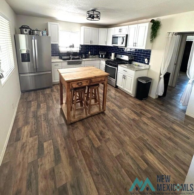 Kitchen featuring appliances with stainless steel finishes, white cabinets, backsplash, dark wood finished floors, and a textured ceiling