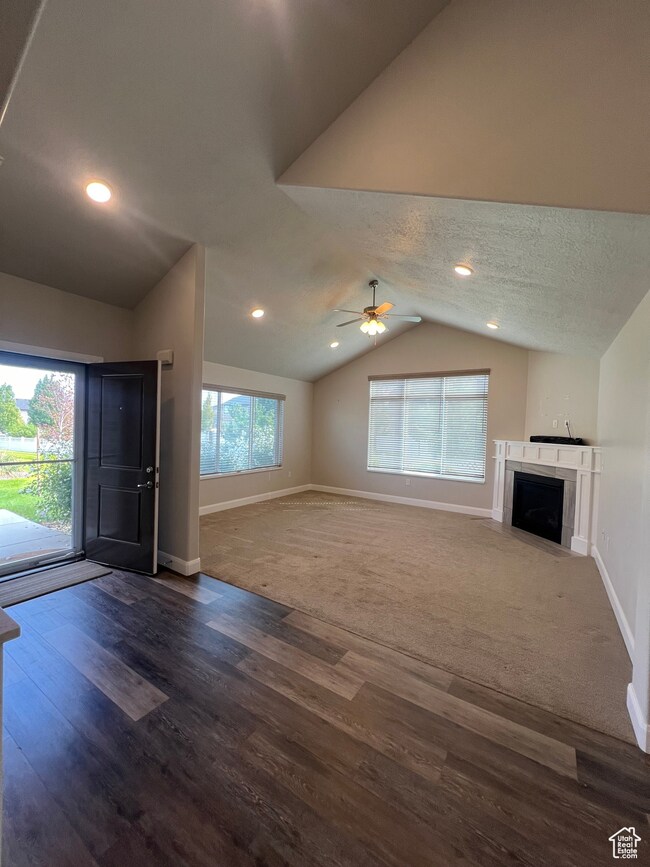 Unfurnished living room featuring lofted ceiling, a textured ceiling, a fireplace with flush hearth, dark wood-style floors, and recessed lighting