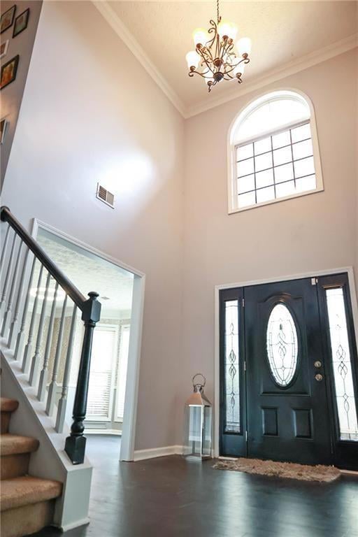 Entryway featuring crown molding, a towering ceiling, stairs, wood finished floors, and a chandelier