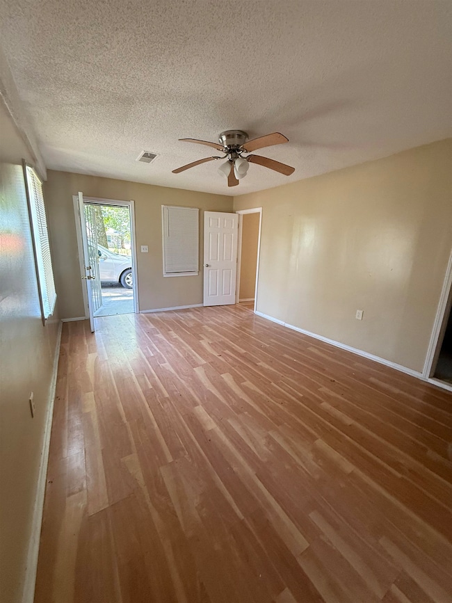 Unfurnished living room featuring light wood-type flooring, a textured ceiling, baseboards, and a ceiling fan