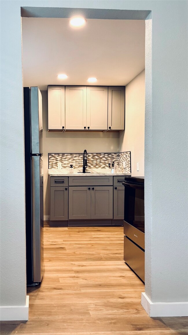 Kitchen featuring stainless steel appliances, gray cabinets, tasteful backsplash, light wood-type flooring, and recessed lighting