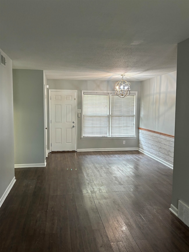 Unfurnished dining area featuring a chandelier, dark wood finished floors, and baseboards