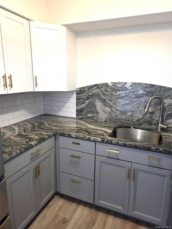 Kitchen with gray cabinets, light wood-style floors, dark stone countertops, tasteful backsplash, and white cabinetry