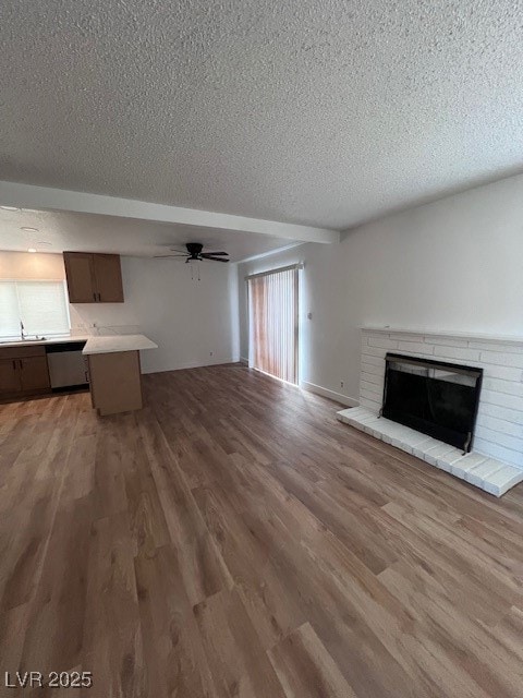 Unfurnished living room with a brick fireplace, a textured ceiling, a ceiling fan, and light wood-style flooring