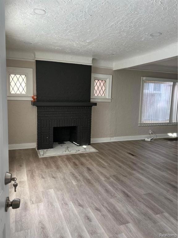 Unfurnished living room with a textured wall, wood finished floors, a fireplace, and a textured ceiling