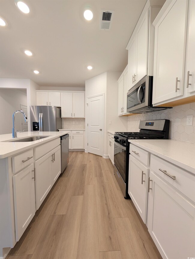 Kitchen featuring tasteful backsplash, stainless steel appliances, white cabinets, recessed lighting, and light wood finished floors
