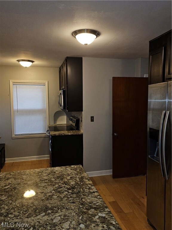 Kitchen featuring dark brown cabinets, light hardwood floors, refrigerator, stove, and dark stone countertops